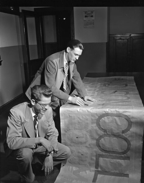 Members of the advertising committee for the Madison Business College's spring formal are working on a huge streamer sign for the party. Seated at left is Charles Meier, 416 North Murray Street with Bill Dunnett, Westport, standing at right. The college, located at 215 West Washington Avenue, will hold its annual dinner and dance at Club Chanticleer, Middleton.