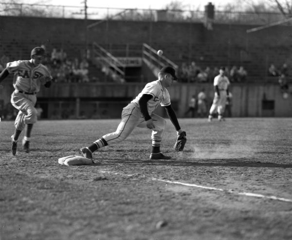 Gordie (Gordon) Hanson of Madison East high school runs safely to first base.  Bob King of Madison Central high school plays second base. The ball bounced off of King's mitt and is shown above his head.