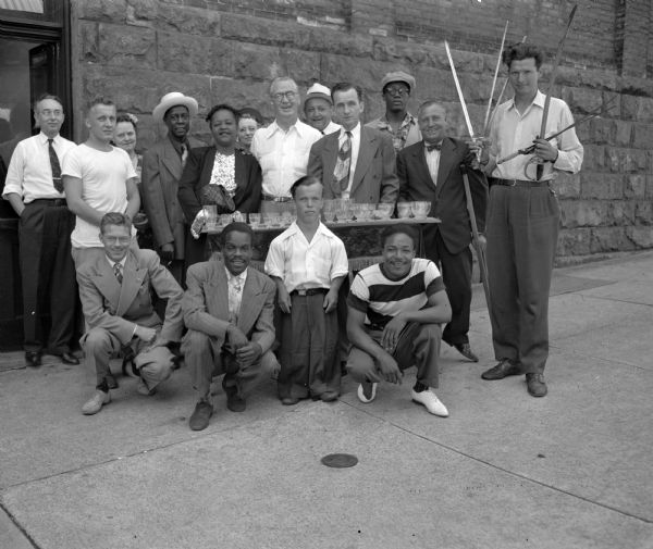 Group portrait of Roundy Couglin and members of the Dodson Imperial Shows at Camp Wawbeek, where they had gone to entertain the 93 children camping there. Front row, left to right: Harold Saxton, driver; Flash Ford, tap dancer; Poodoo, fire eater; "Jigsaw" Jackson, dancer.  Back row left to right: Joe LaCrosse, and Chuck Doring, drivers: Mrs. Goodman, Roundy's secretary; Butter Beans and Susie, comedy dance team; Mrs. Norman Wang, Fun Fund committee member; Roundy; Chick Franklin, manager of Imperial Shows; Harold Smith, water glass musician: John Perry, pianist; the Great LeRoy, magician; and holding four swords is John W. Dunning, champion sword swallower.