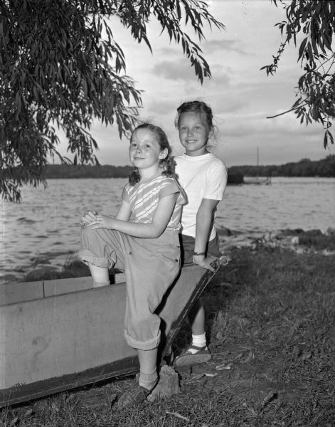 Two girls at Brownie Day Camp at Burrows Park. Standing near a boat on the shore of Lake Mendota is Shelia Sullivan, left, daughter of Mr. and Mrs. J.J. Sullivan, Sun Prairie; and Virginia Holmes, right, daughter of Mr. and Mrs. H.F. Holmes, 244 East Johnson Street.