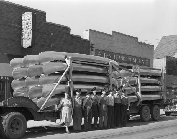 A truckload of canoes in front of Madison Marine Service, 2102 Atwood Avenue, with eight employees standing in front. In the background is the Ben Franklin store, at 2110 Atwood Avenue.