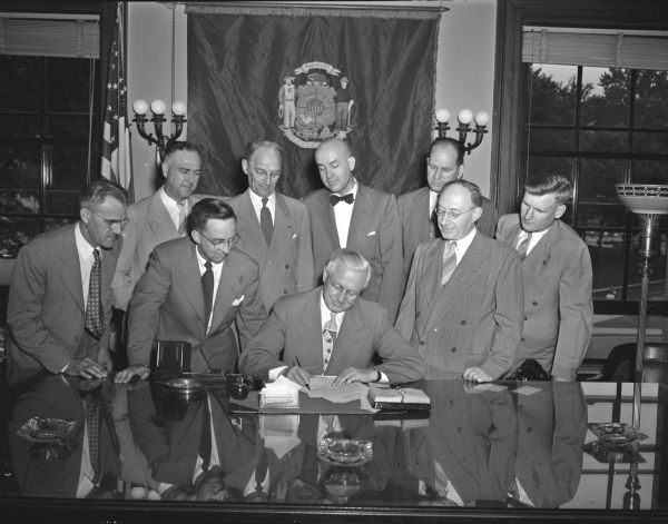 Governor Rennebohm signing a bill with eight men witnessing.