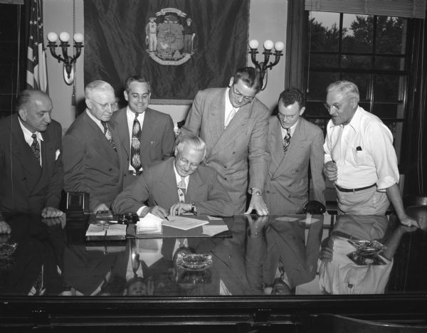 Governor Rennebohm signing a bill with six men witnessing.