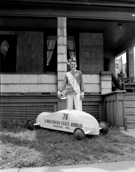 Frankie Meyer, the 1948 Soap Box Derby champion, stands next to his Wisconsin State Journal-sponsored racer.  He is wearing the shirt and helmet given to him when he competed at Derby Downs in Akron, Ohio the previous year.