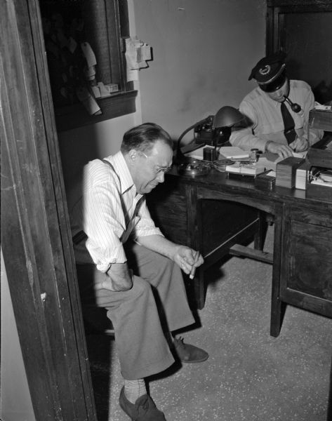 Julius J. Jackson, 1049 East Johnson, seated, with Acting Lieut. Robert O'Brien of the Madison police department in the background. Jackson is the husband of Sadie Jackson, recently murdered.