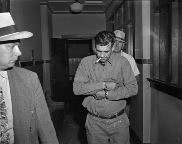 George "Butch" King in handcuffs, after being questioned for the murder of Sadie Jackson, wife of Julius J. Jackson. In the background is Detective Captain Harry L. Milsted.