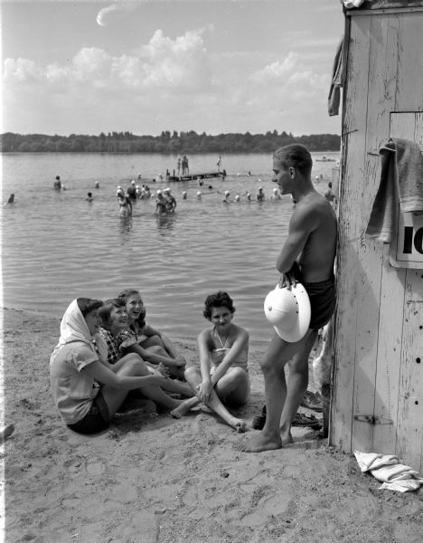 Bob Trotalli, a recent graduate of West High School, has a summer job as a life guard at the Willows Beach on Lake Mendota. He is shown talking to Betsy Miller, Alice Corcoran, and Gayle Grelle, all seniors at West High School, and Peggy Ishmael, a sophomore at the University of Wisconsin.