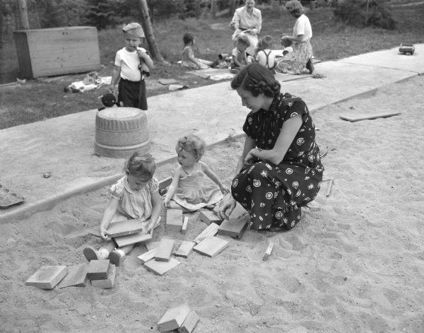 Mrs. H.E. Colbert supervises her daughter, Bonita, and Susan Hickey, both 2 years old, as they play in a sand pile at one of the play areas with wooden blocks made by the fathers of the community.