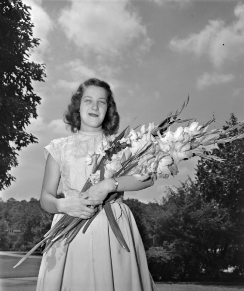 Jeanne Flad, daughter of Mr. and Mrs. John J. (Nell) Flad, Shorewood Hills, holding an armful of gladioli similar to the ones that will be displayed in the eighth annual show of the Madison chapter of the Wisconsin Gladiolus Society. Miss Flad's father is president of the Madison chapter of the Gladiolus Society.
