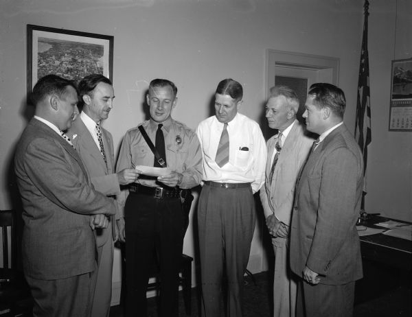 Lieut. Walter Thompson, an officer with the Madison police force, receiving the $650 Kemper Foundation fellowship check to attend the traffic police administration traffic institute in Evanston, Illinois. Lieut. Thompson is one of eight police officers from throughout the country to receive the award. Left to right: L.W. Hagerup, representing the Kemper foundation; N.C. Lerdahl, secretary-treasurer of the Reitan-Lerdahl Mutual Casualty Company, Chicago, who is presenting the check; Lieut. Thompson; City Manager Howell; Harold B. Shier, president of Reitan-Lerdahl, and Police Chief Bruce Weatherly.