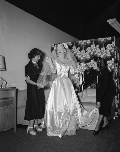 Co-owners Eunice Mills (left) of 823 University Avenue, and Mrs. Ron (Ruth) Rosa of 305 Merrill Crest Drive arrange a satin wedding gown and veil on a mannequin at their bridal shop, located at 507 State Street.