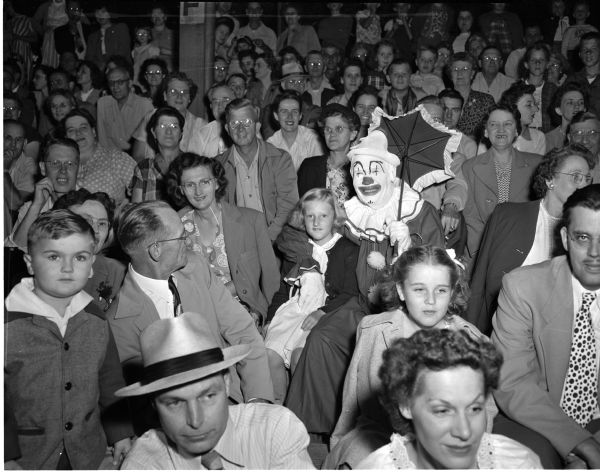 A clown (Bill Kemmel) mingles in a large crowd at Breese Stevens Field at the sixth annual softball "extravaganza" between the Zor Shrine and the Knights of Columbus. A crowd of 7,635 spectators was reported to have attended the clown game.