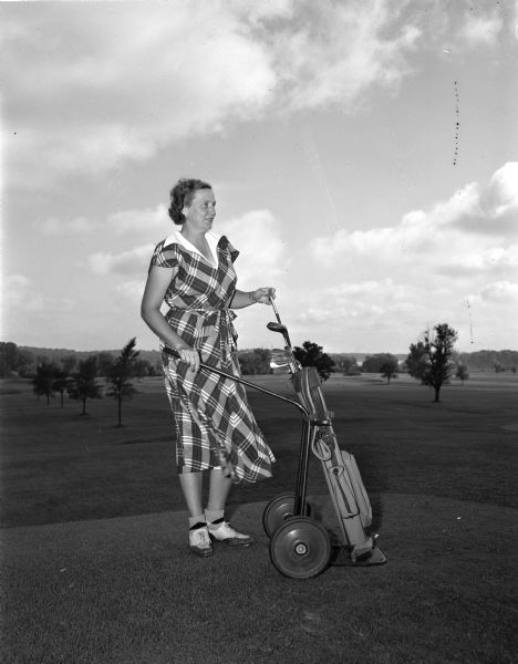 Mrs. Ralph E. (Mariel) Campbell of 133 Manitou Way, chair of the women's organization of the Nakoma Golf club, standing on the course with a bag of golf clubs. The organization is sponsoring their annual Guest Day.