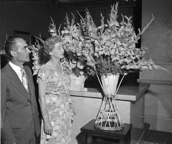 Theodore Woods and Mrs. T.R. (Madeline) Hefty admiring a vase of "Madeline Hefty" gladioli at the Madison gladiolus society's eighth annual show. Mr. Woods developed the variety over a six year period and named it for Mrs. Hefty. The red flower was to be introduced to the buying public in the fall and featured on the catalog cover of a least one national flower grower.