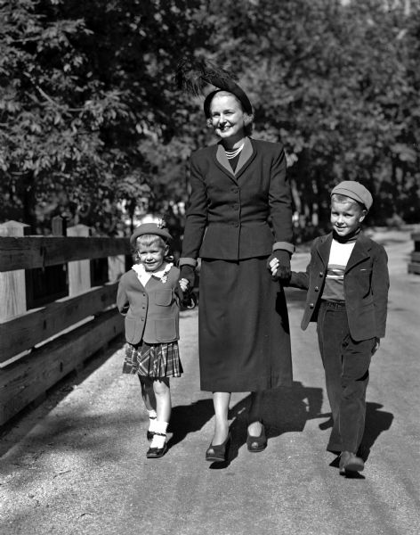 Mrs. Donald O. (Faye) Nelson with her children, Tracy and Timmy, walk over the Rustic Bridge in Shorewood Hills while modeling new autumn fashions.