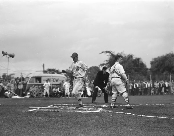 Shortstop Herb Hellenbrand, left, crosses home plate for the first run of the game as Cross Plains defeated Waunakee, 6-2. In the background is a van with a sign on the side that reads: "WFOW."