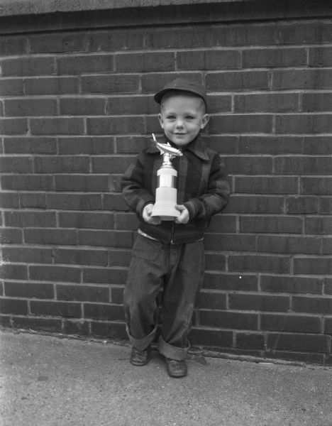 Ronald Rutlin of 1726 Helena Street holding a fishing trophy while standing in front of a brick wall. He was awarded the trophy by the Yahara Fisherman's Club for being the smallest fisherman and catching a fish at their fishing contest for kids.