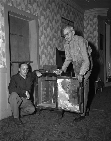 Joseph C. Schabo, the watchman who lives in the Madison American Legion clubhouse at 110 East Wilson Street, is shown at left examining one of two safes that were robbed by three safecrackers who tied him to a sofa during the robbery. At the right is janitor William A. Tucker who rescued Schabo when he arrived at work the following morning.