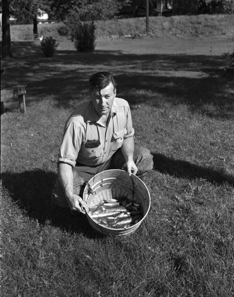 Al Koppenhaver, a game warden for the Wisconsin Department of Natural Resources, holding a bucket of dead fish that were removed from the Yahara River below the Johnson Street bridge. The fish were evidently killed by industrial wastes that entered the river from a storm sewer.
