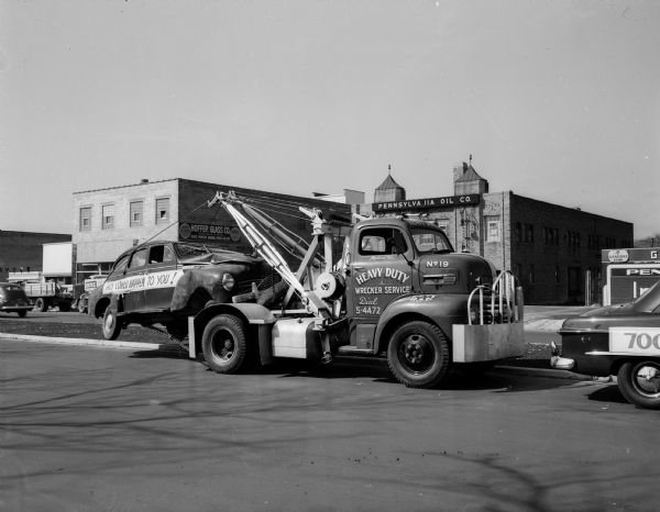 A Heavy Duty Wrecker Service tow truck towing a wrecked car with a banner on the side reading "THIS COULD HAPPEN TO YOU!" during the Kayser safety parade in the 700 block of East Washington Avenue. The parade is part of a $100,000 Car Safety Contest, during which any car, regardless of make, is elibible for a free safety check at any Ford dealer.