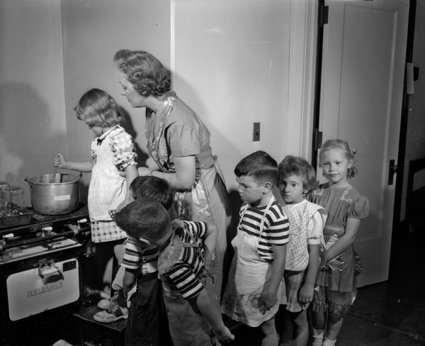 Randall Elementary School kindergartners are shown making applesauce under the supervision of their teacher Marguerite Drew. Stirring the pot is Patty Hurlbut, daughter of Mr. and Mrs. Robert Hurlbut, 1616 Madison Street. Waiting in line to take their turn are left to right: Ricky Radder, son of Mr. and Mrs. Howard Radder, 3323 University Avenue; Richard Rosaldo, son of Mr. and Mrs. Renato Rosaldo, 322 North Blackhawk Avenue; Roberta Fox, daughter of Mr. and Mrs. George T. Fox, 2210 Rugby Row, and Carol Thompson, daughter of Mr. and Mrs. Richard T. Thompson, 4206 Bagley Parkway.