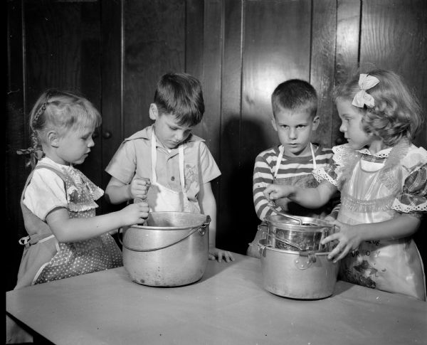 Randall Elementary School kindergartners are shown making applesauce under the supervision of their teachers Marguerite Drew and Lois Griskavich. Pictured putting apples through a food mill are, left to right: Sheryl Brettingen, daughter of the Adolph Brettingens, 4329 Bagley Parkway; Pat Kelly, son of Dr. and Mrs. Stuart Kelly, 315 Virginia Terrace; Richard Heugel, son of the Freeman Heugels, 4106 Euclid Avenue, and Ann Liddle, daughter of the Clifford Liddles, 1909 Regent Street.