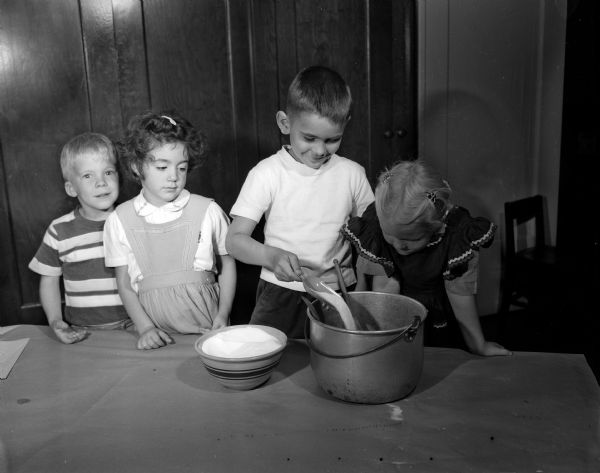 Randall Elementary School kindergartners are shown making applesauce under the supervision of their teachers Marguerite Drew and Lois Griskavich. Adding sugar to the applesauce are, left to right: Roald Erickson, Polly Brodie, John Thompson holding the scoop, and Karen Tanner.