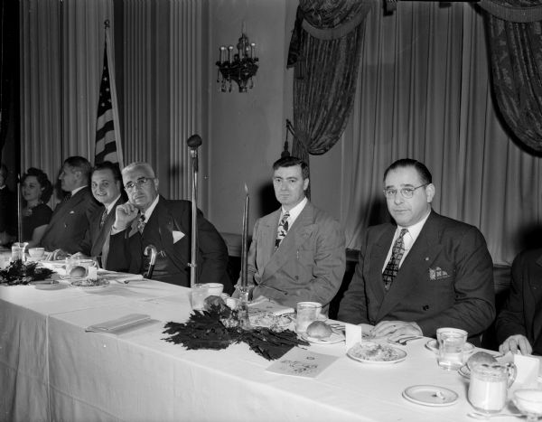 Speakers at the Columbus Day dinner, sponsored by the Madison chapter of UNICO National at the Hotel Loraine, sit at a table with a tablecloth and place settings. Left to right are Matt Morrelli, St. Paul, Minnesota, national vice-president of UNICO; A.R. Sanna, Sr., Madison; Peter Fiore, general chairman of the banquet and William C. Davini, St. Paul, Minnesota, master of ceremonies and past national president.