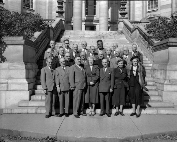 Group portrait of the twenty three members of the Governor's Commission on Human Rights standing on the steps of the Capitol Building.
First row, left to right:  Professor Selig Perlman, Madison; Bert C. Broude, Milwaukee; August Reisweber, Milwaukee; Rebecca Barton, Madison, executive secretary; Dr. Joseph Barron, Milwaukee; Margaret Chenoweth, Janesville; and Mrs. George Thompson, Hudson. Second row: Rev. Alfred W. Swan, Madison; Rev. Franklin Kennedy, Milwaukee; County Judge Fred M. Evans, Madison; Rev. Francis McDonnell, Madison; and Bruno Bitker, Milwaukee.  Third row: G.W. Bannerman, Wausau; I.F. Nelson, Kaukauna; Maurice H. Terry, Milwaukee; Sidney L. Goldstine, Madison and Leonard J. Kleczka, Milwaukee. Fourth row:  Allan MacAndrews, Madison; Herman Steffes, Milwaukee; O.A. Jirikowic Milwaukee; James W. Dorsey, Milwaukee; Dr. R.C. Williams, Whitewater; and A. Zellmer, Wisconsin Rapids.