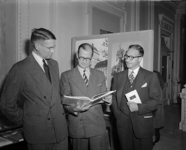 Professor Gilbert H. Doane, (left) director of the University of Wisconsin libraries, is shown admiring one of more than 300 Swiss publications which are outstanding examples of work done in 1948 by Swiss Publishers. With Professor Doane are Dr. William Schilling (center) Swiss consul-general at Chicago and O. Goetz, chancellor of the Chicago consulate.