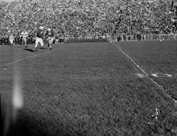 Halback Rollie Strehlow (40) running for a touchdown against Navy during the football game between the University of Wisconsin and the Navy Midshipmen at Camp Randall. Also in the shot are Wisconsin's Jerry Schaefer (18) and Navy's Bill Steele (62).