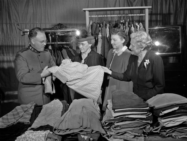 Major Frank Genge, director of the Salvation Army in Madison, telling three women's division volunteers of the Community Chest about the weekly clothing sales. The women are, (from left): Mrs. Elsie Abraham, Mrs. J.V. (Naomi) McEvilly, and Mrs. C.D. (Edna) SeCheverell.