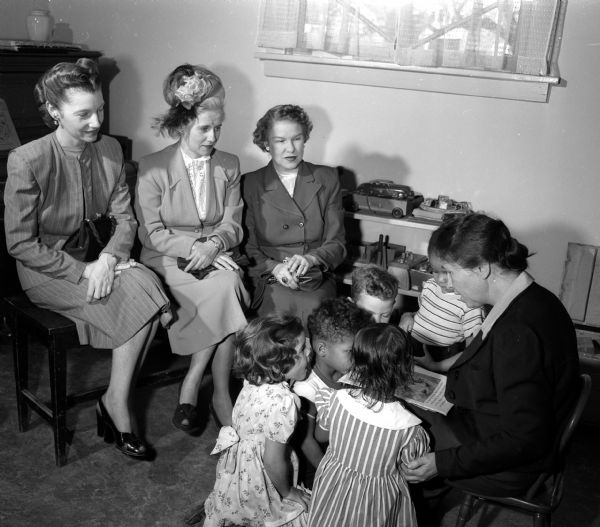 Mary Lee Griggs reads to some of her pupils at the Neighborhood House while three women's division volunteers of the Community Chest look on. From left are: Mrs. Joseph (Phyllis) Gervasi, Mrs. Sal (Josehine) Maglio, and Mrs. I.C. (Leone) Rheaume.