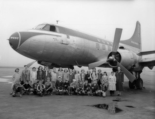 A group of sixth graders, from Lowell School, are shown with a Northwest Airlines plane at Madison's municipal airport as a part of their study of transportation and communication.