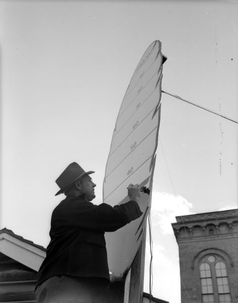 Peter H. Norg, executive director of the Four Lakes Council of Boy Scouts (a Red Feather service of the Madison Community Chest), adds some red paint to the 12-foot feather thermometer located next to the city hall at the corner of Wisconsin and Mifflin streets.