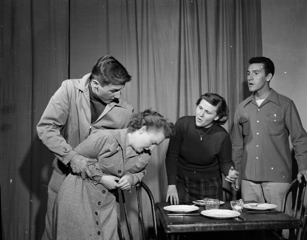 The Madison Blackfriars Guild is shown rehearsing a scene from Tennessee Willliams' play," The Glass Menagerie".  Here, Laura (Patricia McKune) collapses as she faces the "Gentleman Caller" (Eugene DeCaprio) far right, with whom she had been in love. Holding her is her brother, Tom (Eugene Van Hekle), and at the table is her mother, Amanda (Lucy L. Nes).