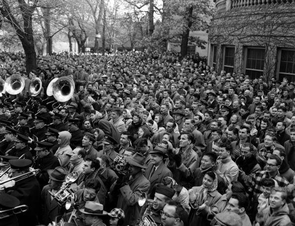Elevated view of a large crowd of people gathered on the University of Wisconsin Union Terrace to listen to a speech by Prime Minister Pandit Jawaharlal Nehru of India. The crowd includes U.W. band members in uniform.