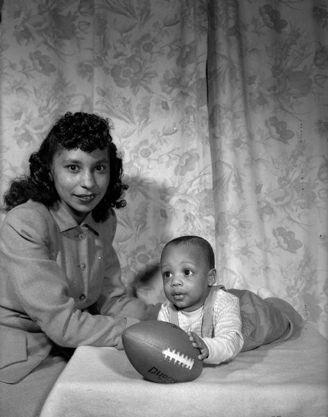 Oletha Withers poses with her 5-month-old son, Eddie Withers III, who is holding a football.  They are the wife and son of Eddie Withers, Jr., half-back on the University of Wisconsin football team.