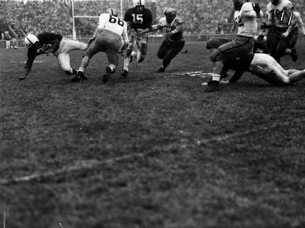 University of Wisconsin running back Gwynn Christensen (#15) carries the ball against Iowa in their game at Camp Randall. Iowa players trying to make the tackle are Earl Banks (#73) and Joe Bristol (#66).