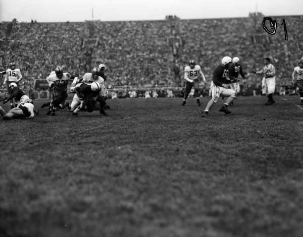 University of Wisconsin running back Gwynn Christensen (#15) carries the ball against Iowa in a football game at Camp Randall. Iowa players making the tackle are Earl Banks (#73) and Hubert Johnson (#37).