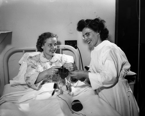 Doris Trameri of 568 Park Lane, previously diagnosed with tuberculosis, posing in her former room at Lake View Sanatorium while knitting argyle socks. She is talking with Caroline Schnering, occupational therapist.