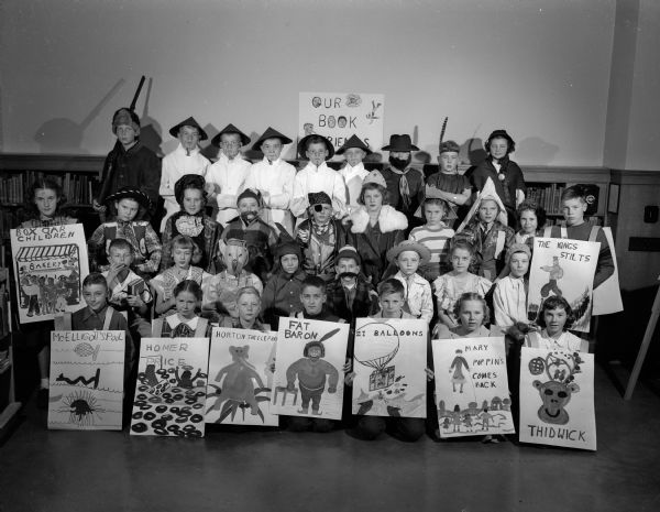 Marquette school children posing for a group portrait while dressed up to represent their favorite literary characters. Some of the children are holding signboards illustrating scenes from best-liked books.