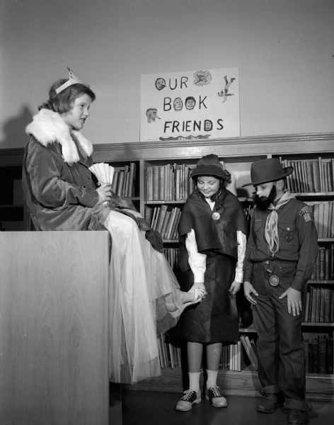 Emiline Curless, dressed as Mrs. Piggle-Wiggle, and Lance Felly, dressed as General U.S. Grant, admire Cinderella's slipper on the foot of Beverly Hoppmann at a celebration of National Book Week at Marquette School.