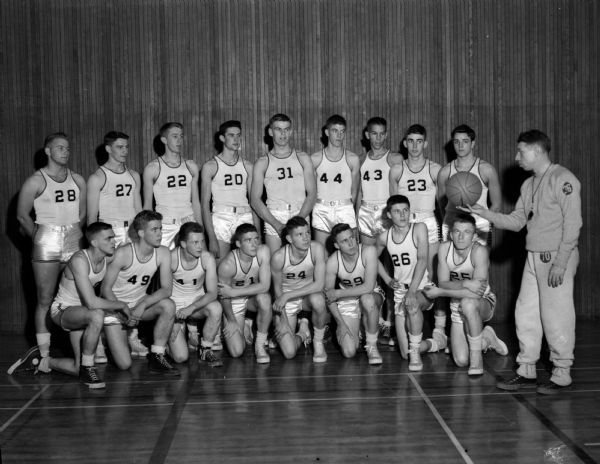 Group portrait of East High School boy's basketball team. Coach Milt Diehl demonstrates a lay-up shot technique.