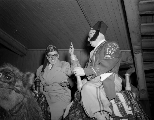 Bellamy Seals (right), captain of the camel patrol, watching as Shrine leader Harold Lloyd tries out one of the camels. The Hollywood producer was in Madison as Imperial Potentate of the Ancient Arabic Order, Nobles of the Mystic Shrine of North America.