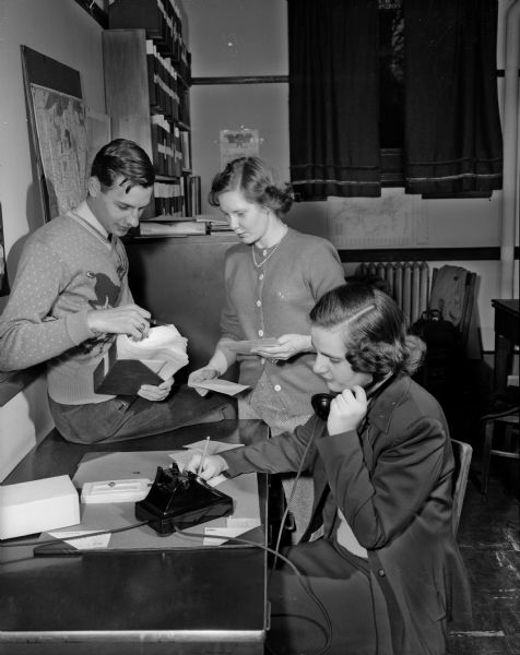 University of Wisconsin recreation student Mary Ann Busch, Eagle River, receives a call for a student to lead games at a little girl's club. Glenn Gritzmacher, Wausau, left, and Betty Hovey, Madison, check through the recreation service bureau's file cards to find a student qualified for the job.
