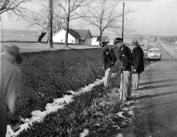 County Traffic officers, E. W. Kelzenberg and Emil Schmale, and Evan Chambers of the state crime laboratory looking at the death scene of Bernice Johnson. The site is a ditch next to Fish Hatchery Road in front of the Ernest Buri home on the A.W. Gallagher farm, near a pasture where she had been beaten and abandoned.