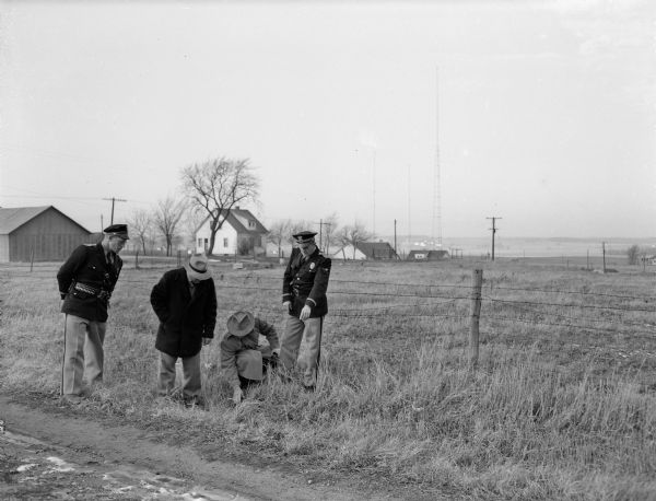 County officers and state crime lab officials searching for clues in the pasture near Fitch Hatchery road, where Bernice Johnston was beaten and abandoned. The investigators are, left to right: County Officer Emil Schmale: Evan Chambers and Don M. Harding of the crime laboratory; and Officer E. W. Kelzenberg.