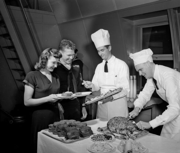 Charles H. Haynie, executive officer, and Arthur G. Field (right),  commanding officer of the reserve unit, are shown serving food to Hobert & Donna Frank at the United States Naval Reserve Surface Division 9-212 surprise party. The party was given by the officers for the enlisted men at the new training center, located at 1046 East Washington Avenue. The training center has a complete duplication of the bridge of a ship.