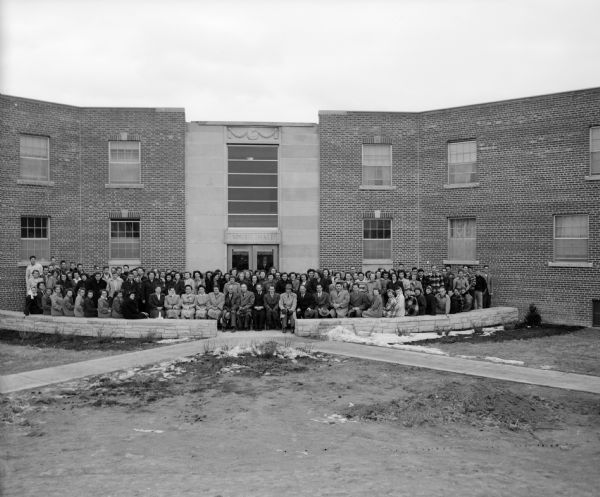 A group of people, possibly faculty and students, stand in front of the newly built South Hall of the Wisconsin Academy.  The academy was formerly known as Bethel Academy and was founded in 1899 by the Wisconsin Conference of Seventh-Day Adventists. It was located in Arpin, Wisconsin until moving to Columbus on September 4, 1949 at which time it was renamed.